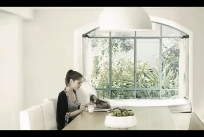 A woman sitting at a dining table next to a large window featuring smart glass for interior design overlooking a garden.
